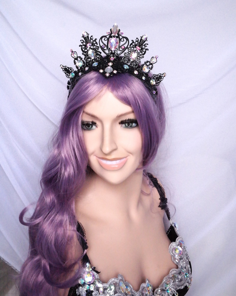 May include: A black wire crown with iridescent rhinestones and black beads. The crown is worn by a person with purple hair.