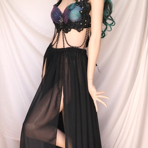 May include: A black sheer maxi skirt with a high slit and a black beaded belt. The skirt is paired with a black and purple sequined bra top with black lace trim.