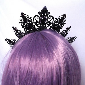 May include: Black crown hair comb with intricate details and black gemstones. The comb is worn on a purple wig.
