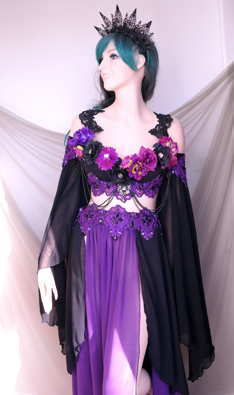 May include: A black and purple fantasy costume with a matching crown. The outfit features a purple bodice with floral accents, a black skirt, and long, flowing sleeves. The crown is black with decorative spikes.