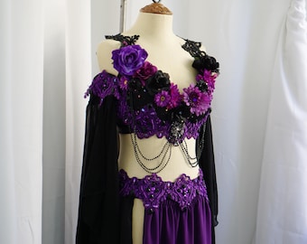 May include: A purple and black belly dance costume on a mannequin. The top is adorned with purple and black flowers, lace, and beaded accents. The skirt is a deep purple color, and the costume has long black sleeves.