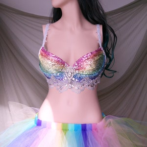 May include: A rainbow sequined bra with a white lace trim and a large rhinestone embellishment in the center. The bra is paired with a rainbow tulle skirt.
