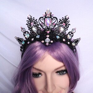 May include: A black metal crown with iridescent pink and white rhinestones. The crown is ornate and has a delicate design.