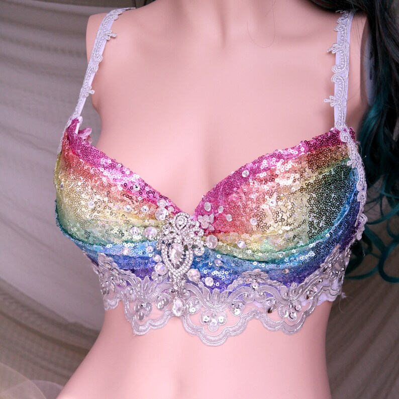 May include: A rainbow sequined bra with a white lace trim and a large rhinestone embellishment in the center.