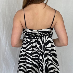 May include: A black and white zebra print mini dress with thin straps and a gathered waistline. The dress has a satin-like finish.