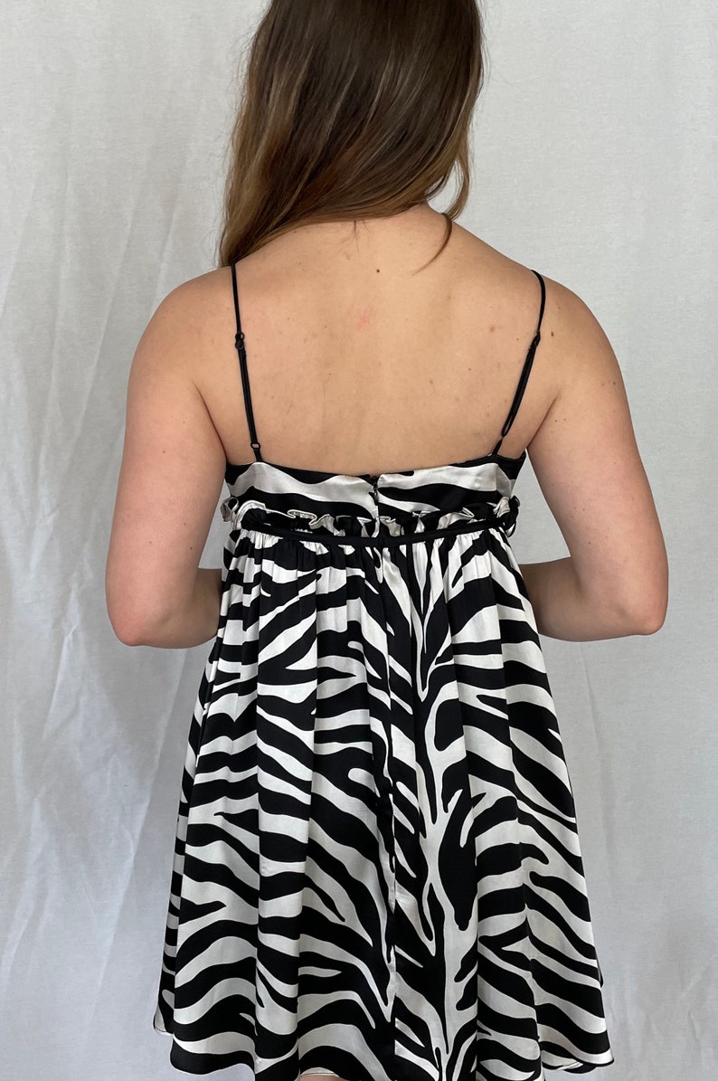 May include: A black and white zebra print mini dress with thin straps and a gathered waistline. The dress has a satin-like finish.