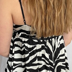 May include: A black and white zebra print top with thin straps. The top has a gathered ruffle at the neckline and a loose, flowy fit.