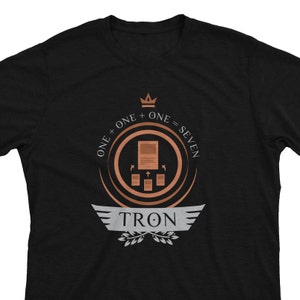 May include: Black t-shirt with a copper-colored logo featuring a crown, the text "ONE + ONE = SEVEN", and the word "TRON" in a stylized font.