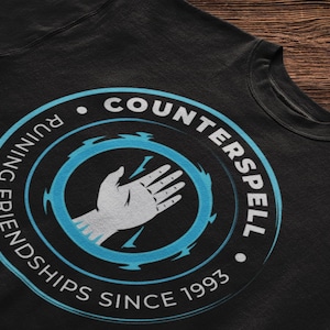 May include: Black t-shirt with a blue and white circle graphic. The circle features a hand with lightning bolts and the text "Counter Spell" and "Friendships Since 1993".