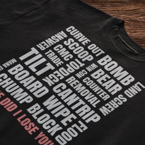 Op de afbeelding: Zwart sweatshirt met witte tekst die "LAND SCREW BEAR BOMB CURVE OUT SCOOP TOP DECK CMC TRADE REMOVAL COUNTER NO. NM  TILT CANTRIP WIPE BOARD BLOCK CHUMP WHERE DID I LOSE YOU" zegt.