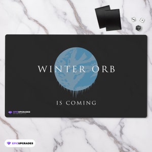 May include: A black gaming mat with a blue and white graphic of a planet with icicles dripping from it. The text "WINTER ORB IS COMING" is printed in white on the mat.