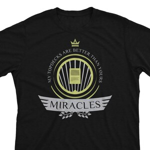 May include: Black t-shirt with a gold and white design. The design features a crown, a circle with a card inside, and the text "My Topdecks Are Better Than Yours" and "Miracles".