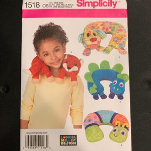May include: A Simplicity 1518 sewing pattern envelope for U.S. one size neck pillows. The front displays a child wearing a red fox neck pillow, alongside illustrations of a floral dog, a blue and green dinosaur, and a patterned caterpillar neck pillow.