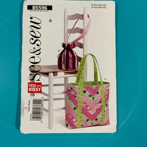 May include: A See & Sew B5596 sewing pattern envelope featuring illustrations of a drawstring pouch and a tote bag. The tote bag has a chevron pattern in pink, green, and floral prints. The pouch is black and pink with a polka dot strap.