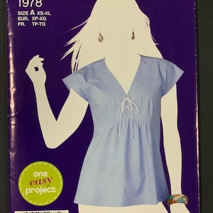 May include: A Simplicity sewing pattern, featuring a light blue top with a V-neck and tie detail. The pattern cover is purple with the text "Simplicity" and "Sew Simple". The pattern number is 1978, with sizes XS-XL.
