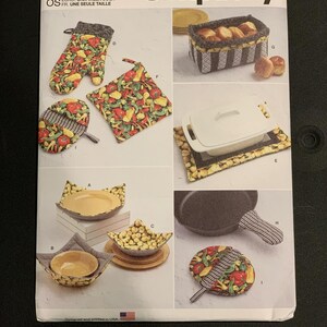 May include: A Simplicity S9365 sewing pattern envelope featuring illustrations of kitchen accessories including an oven mitt, pot holders, bowl cozies, a bread basket, and a skillet handle cover, all showcasing vegetable prints and striped fabric patterns.
