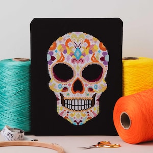 May include: A colorful sugar skull cross stitch pattern on black fabric. The skull is decorated with flowers and swirls in shades of pink, yellow, blue, and green.