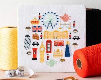 May include: A white canvas with a cross-stitch design featuring iconic London landmarks, including Big Ben, the London Eye, a red double-decker bus, and a red telephone booth. The design is surrounded by a border of red, white, and blue.