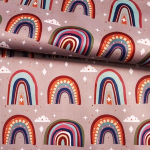 May include: A patterned fabric featuring repeating rainbows, clouds, and diamond shapes on a mauve background. The rainbows are in shades of red, orange, blue, and green. The fabric is folded over in the upper right corner.
