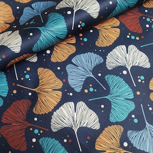 May include: Dark blue fabric featuring a repeating design of ginkgo leaves in white, orange, teal, and light blue. The leaves have detailed vein patterns and are scattered across the fabric. Small coloured dots are also present.