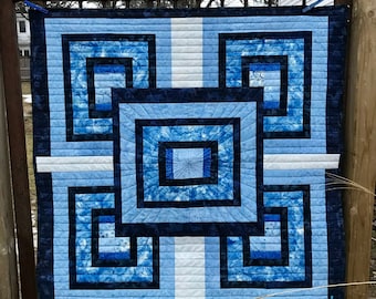 Puede incluir: Un edredón cuadrado con un diseño geométrico en tonos azules y blancos. El edredón presenta cuadrados y rectángulos concéntricos, con un diseño cuadrado central. El edredón se exhibe al aire libre. El texto "mmm quilts" es visible.