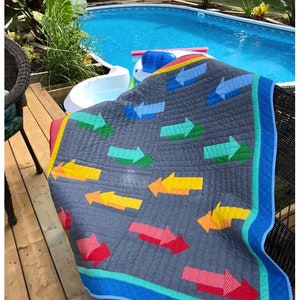 May include: A quilt with a modern design featuring colorful arrows pointing to the right. The quilt is made with fat eighths, fat quarters, and scraps. The quilt is available in baby and throw sizes.