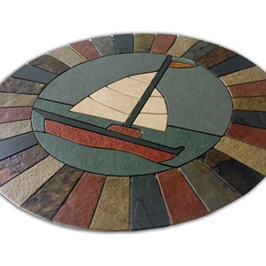 May include: A circular stone mosaic with a sailboat design. The sailboat is made of beige, brown, and black stones. The background is a blue-green color. The outer ring of the mosaic is made of various colored stones.