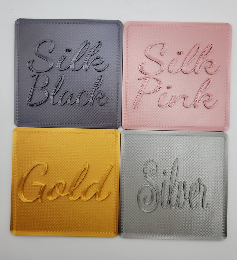 Puede incluir: Cuatro posavasos cuadrados con un acabado texturizado en diagonal. Arriba a la izquierda, gris oscuro con el texto Silk Black. Arriba a la derecha, rosa claro con el texto Silk Pink. Abajo a la izquierda, dorado con el texto Gold. Abajo a la derecha, plateado con el texto Silver.