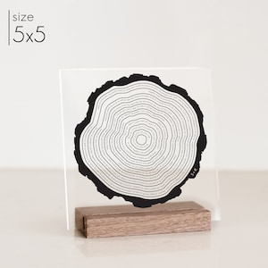 Acrylic tree ring art sign that is printed in black and has a wood stand.