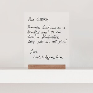 This is a handwritten sign on a white acrylic rectangle that sits in a wooden stand. Sign is sitting on a bookshelf ledge.