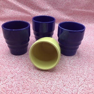 May include: Four ceramic pots. Three are a deep blue with a glossy finish and a stepped design. One is yellow. The pots are arranged on a pink floral patterned surface.