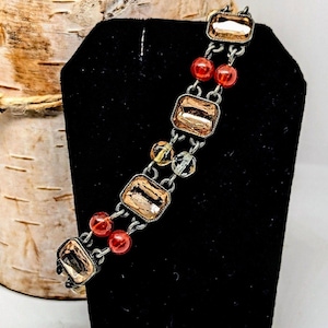May include: A silver chain bracelet with rectangular, clear, faceted glass beads and red round beads.