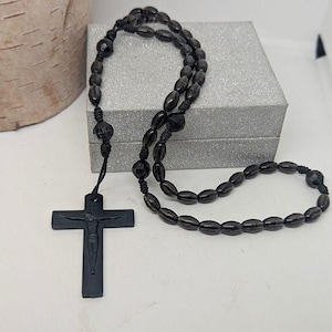 May include: A black rosary with oval beads and a crucifix. The beads are strung together with black string. The crucifix features a detailed depiction of Jesus Christ.