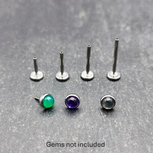 May include: A collection of silver-colored labret studs and posts, with three gemstone studs in green, purple, and gray. The text "Gems not included" is at the bottom of the image.