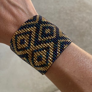 May include: A beaded bracelet with a black and gold geometric pattern. The bracelet is made of small, iridescent beads.