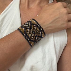 Può includere: Un bracciale a polsino largo con un motivo geometrico. Il bracciale presenta una combinazione di perline dorate e blu navy, creando un contrasto sorprendente. Il design è intricato e dettagliato, mostrando la maestria artigianale. Un accessorio di tendenza.