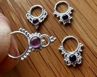 Puede incluir: Tres aros de plata con un diseño circular que presenta detalles metálicos en forma de cuentas y una piedra preciosa redonda de color púrpura engastada en el centro de cada pieza. Los aros de plata tienen un mecanismo de cierre articulado.