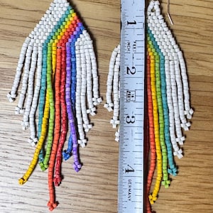 May include: A pair of rainbow beaded earrings with white beads. The earrings are approximately 10 cm long and are measured against a ruler.