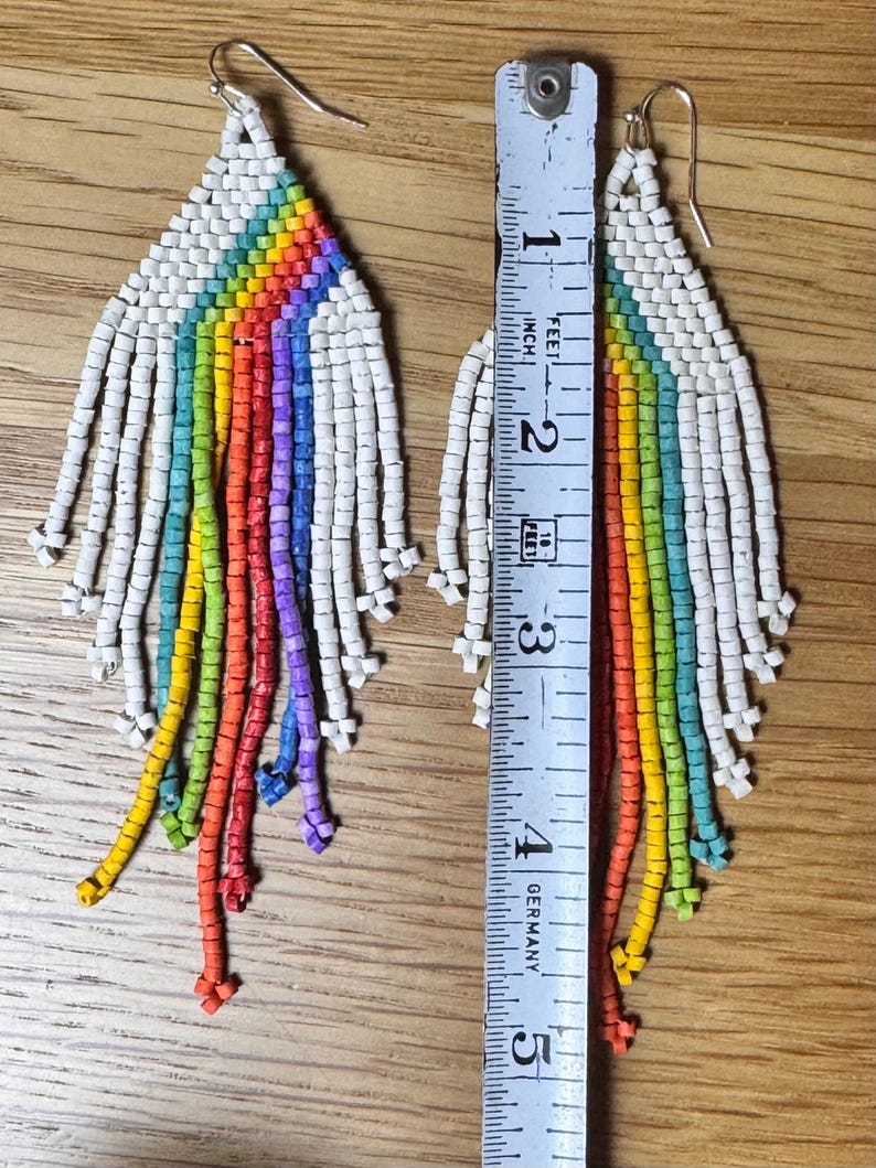 May include: A pair of rainbow beaded earrings with white beads. The earrings are approximately 10 cm long and are measured against a ruler.