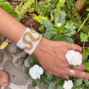 May include: White beaded bracelet with gold beads forming the number "22" on a person's wrist.