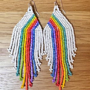 May include: A pair of rainbow beaded earrings with white beads. The earrings are long and dangle, with a rainbow of colours cascading down from the top.