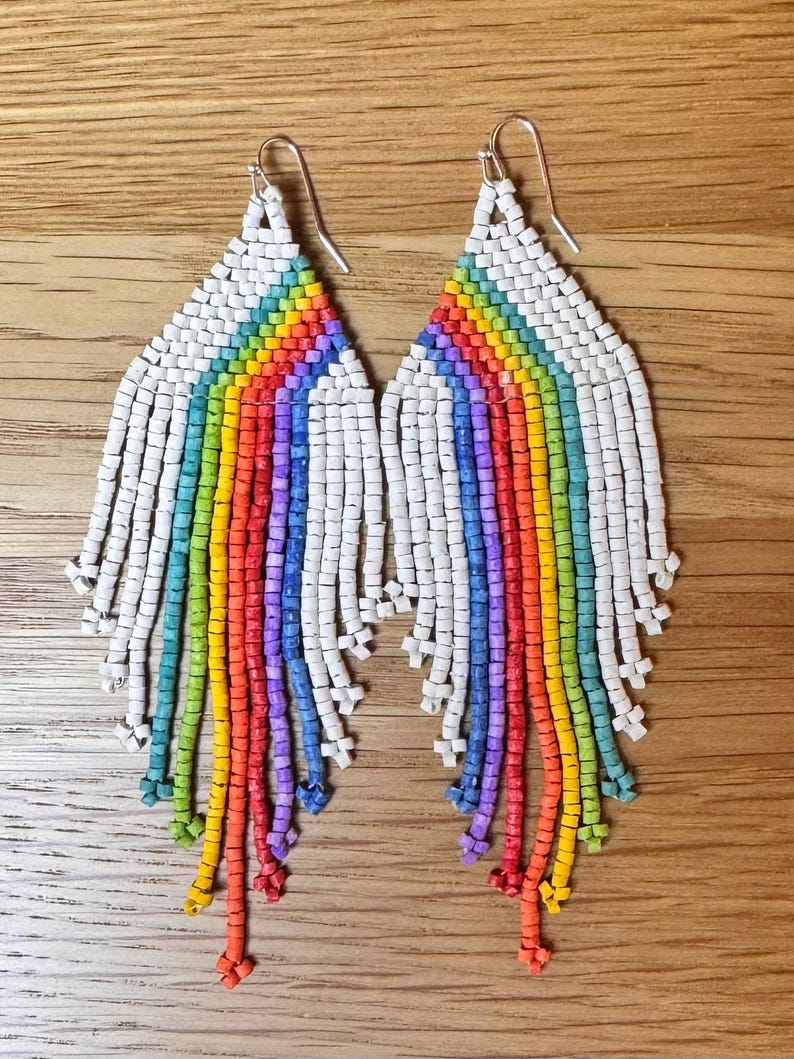 May include: A pair of rainbow beaded earrings with white beads. The earrings are long and dangle, with a rainbow of colours cascading down from the top.