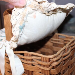 May include: A woven wicker basket with a lid made of white fabric and lace. The lid is lifted to reveal the inside of the basket.