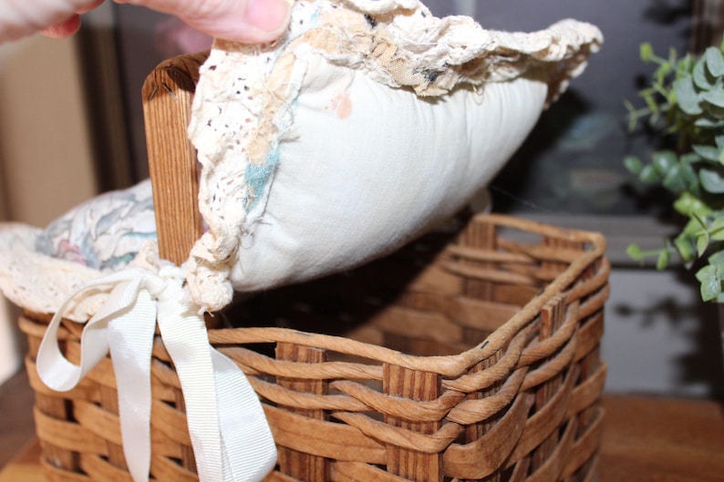 May include: A woven wicker basket with a lid made of white fabric and lace. The lid is lifted to reveal the inside of the basket.