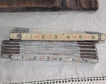 Puede incluir: Dos reglas plegables antiguas, una marcada "STANLEY No. 108" y la otra "EMPIRE SPRING". Ambas reglas son blancas con marcas negras y rojas, midiendo hasta 15 cm. Las reglas están hechas de madera y metal.