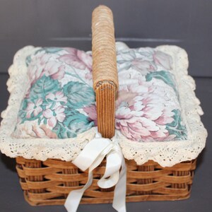 May include: A wicker basket with a floral fabric lining and a white ribbon. The basket has a woven handle and a lace trim.