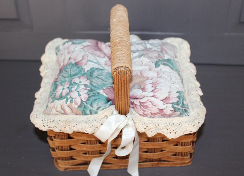 May include: A wicker basket with a floral fabric lining and a white ribbon. The basket has a woven handle and a lace trim.