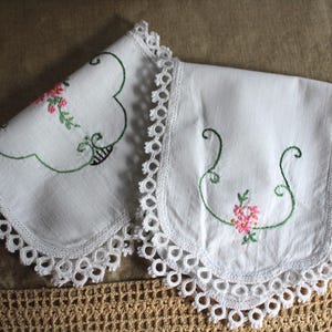 Puede incluir: Dos pañuelos blancos bordados con bordes festoneados y delicados diseños florales. El bordado presenta flores rosas y tallos verdes. Los bordes están adornados con encaje blanco.