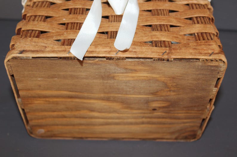 May include: The bottom of a wooden basket with a woven top. The basket is made of natural wood and has a light brown color. The basket is empty.