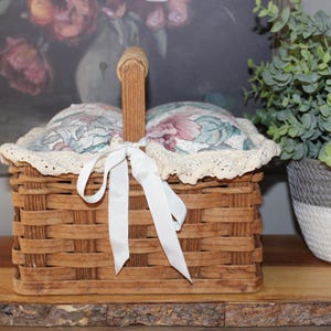 May include: A wooden basket with a floral fabric lining and a white ribbon. The basket has a handle and is sitting on a wooden surface.